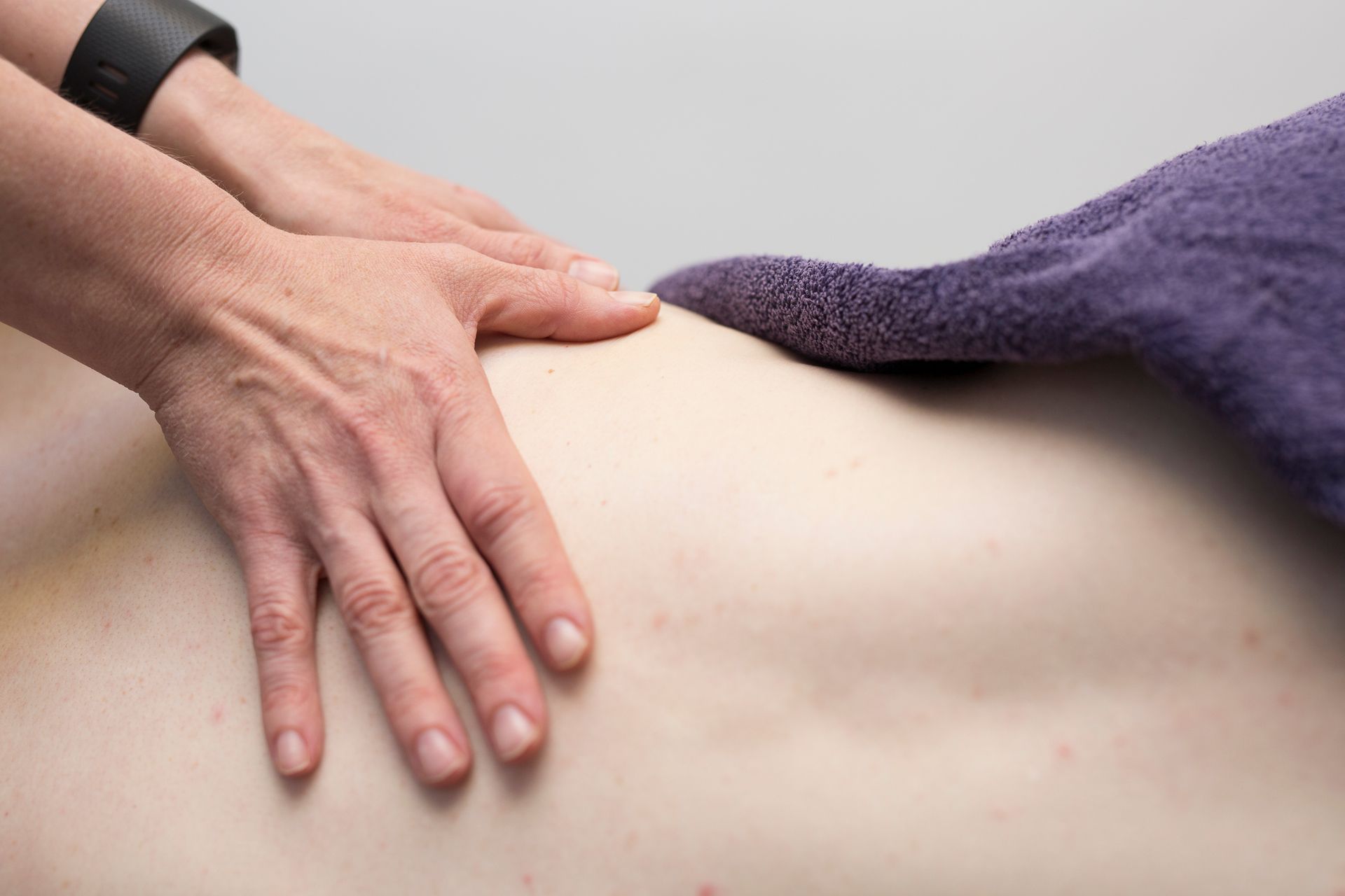 Hands massaging a person's back, next to a purple towel. Hands massaging a person's back, next to a purple towel.