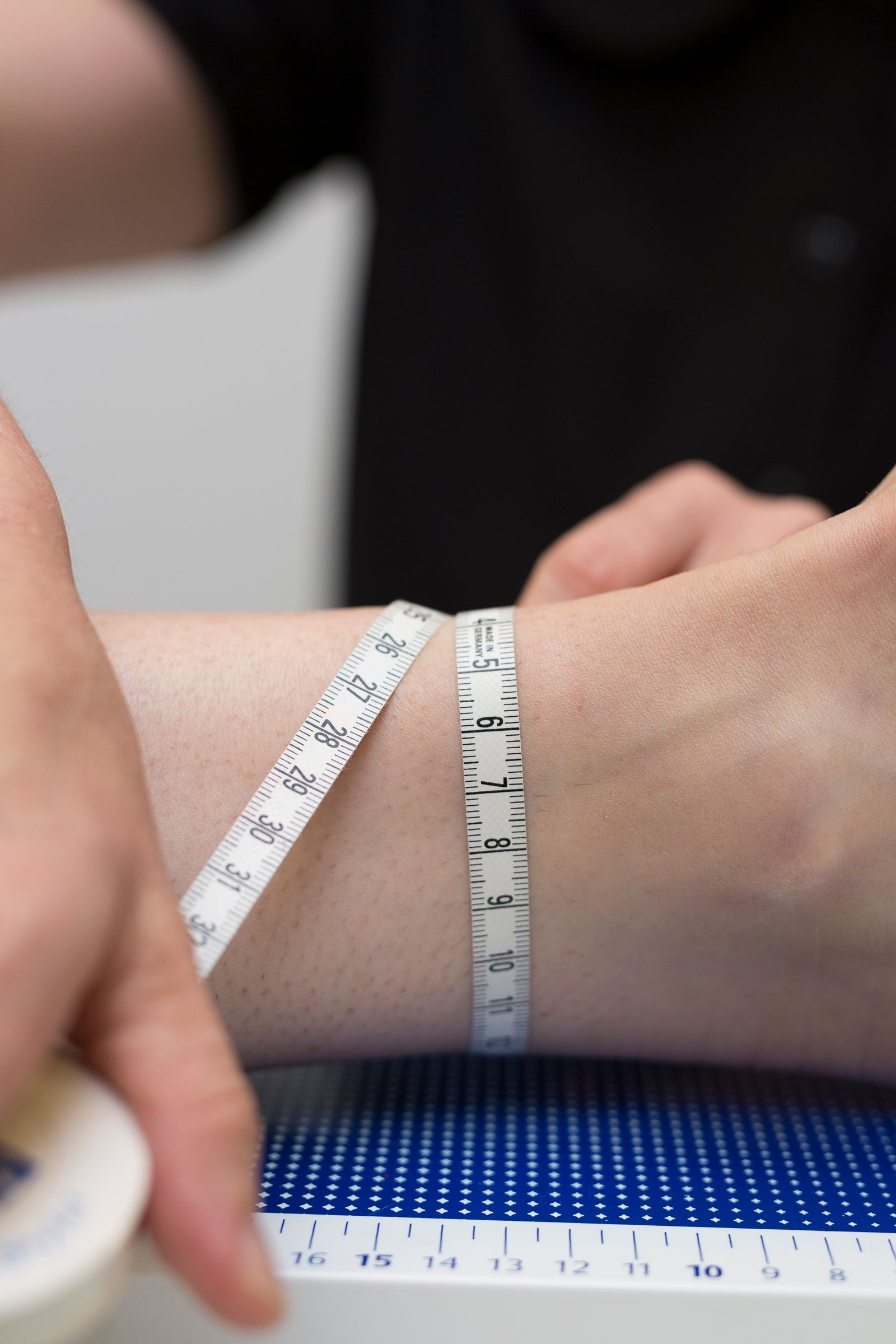 A person's wrist being measured with a white tape measure against a blue surface. A person's wrist being measured with a white tape measure against a blue surface.