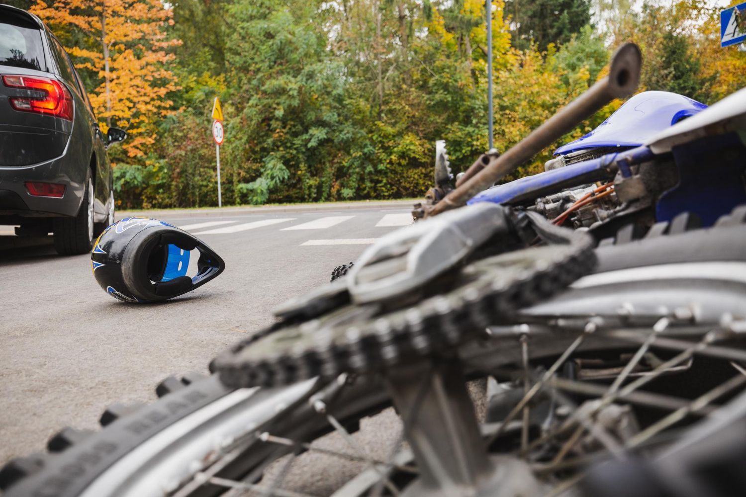 A woman is kneeling down next to a damaged car and looking at her phone.
