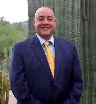 A man in a suit and tie is standing in front of a cactus.