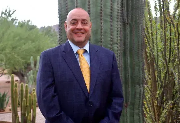 A man in a suit and tie is standing in front of a cactus.