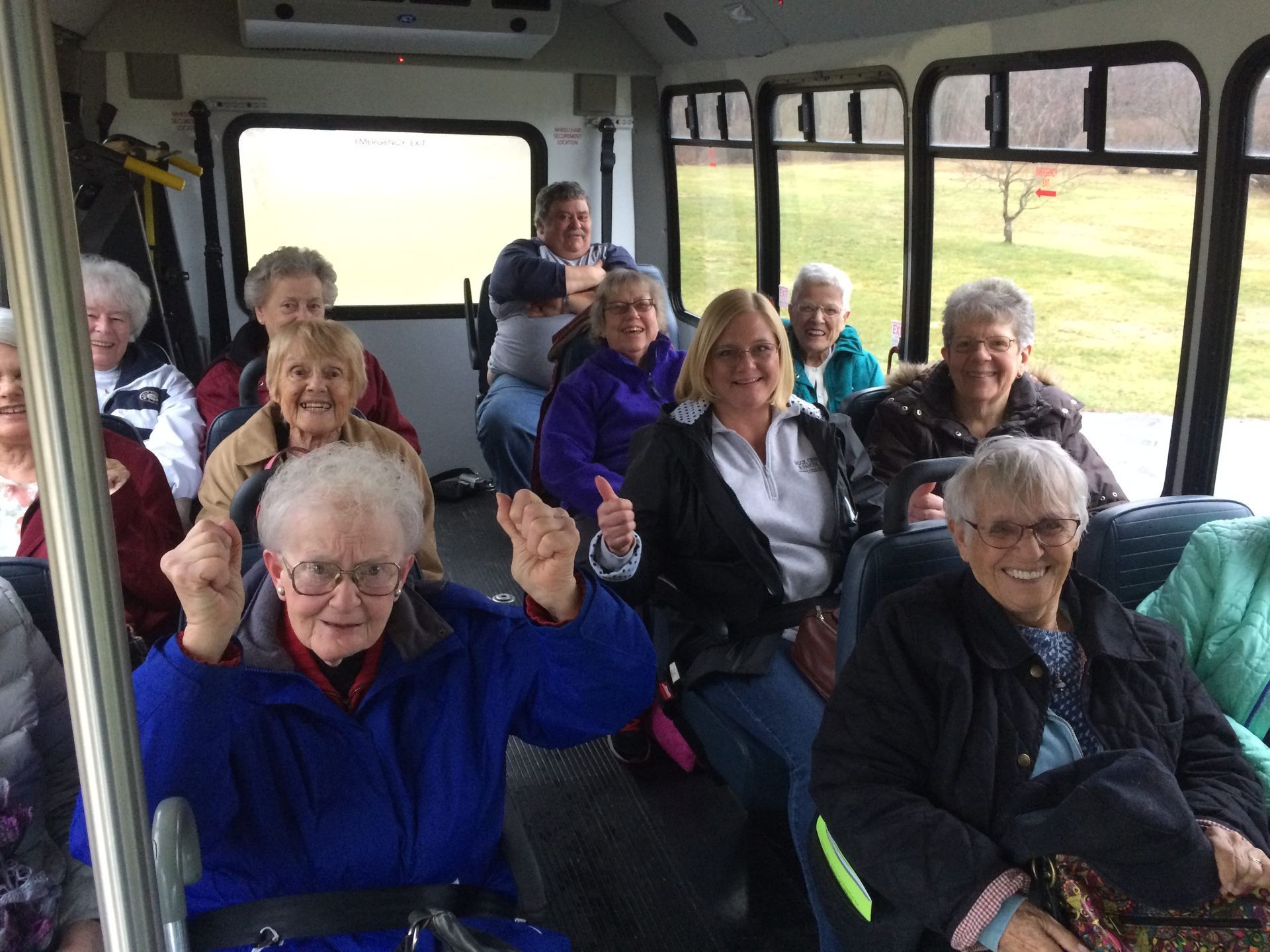 A group of older adults on a bus smiling and looking happy