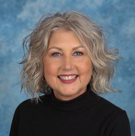 white female smiling at the camera with short grey-blond wavy shoulder-length hair
