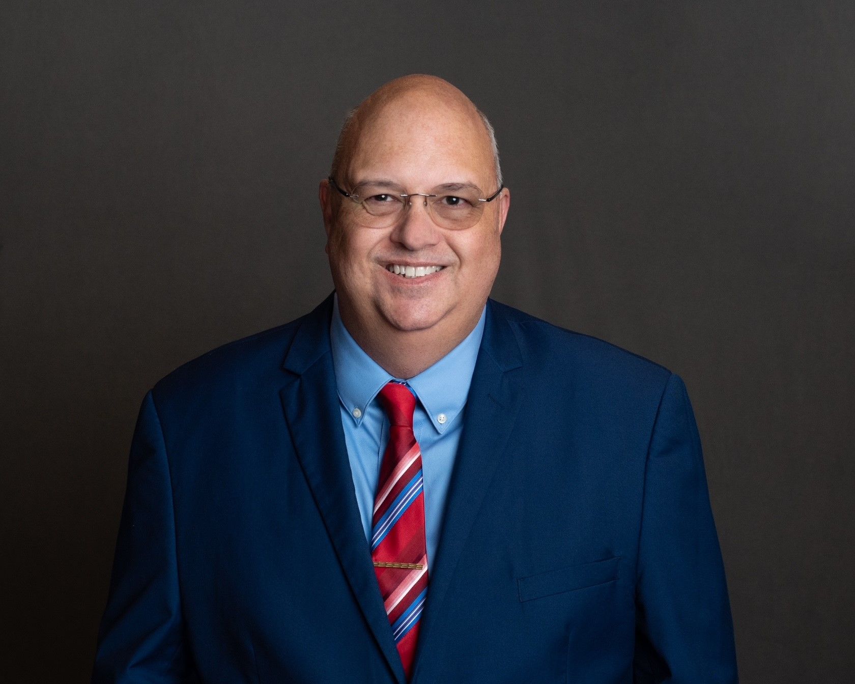 white bald male in a blazer jacket smiling at the camera