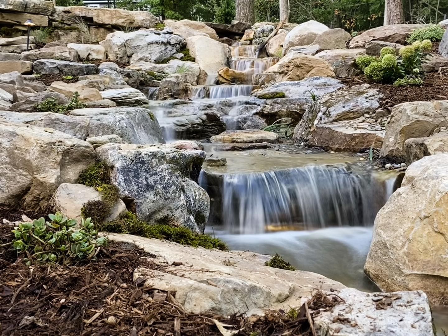 Small cascading waterfall over rocks in a wooded garden stream