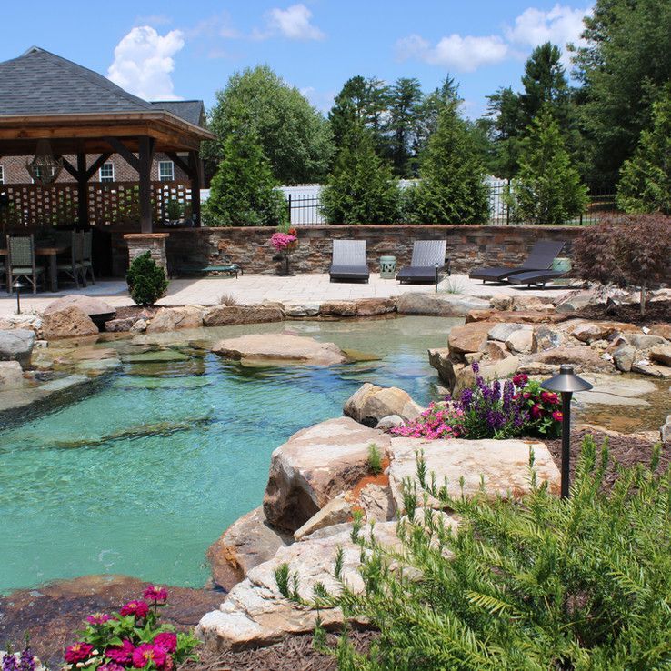 Natural stone swimming pool with turquoise water, rocks, flowers, and lounge chairs beside a gazebo