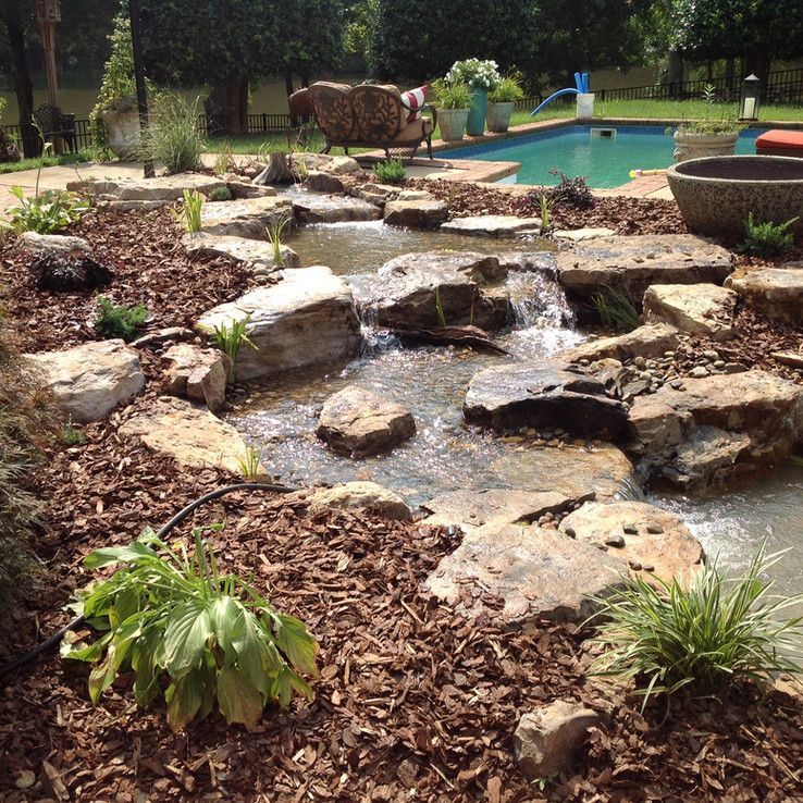 Rock garden waterfall flowing into a backyard pool with plants and stone landscaping