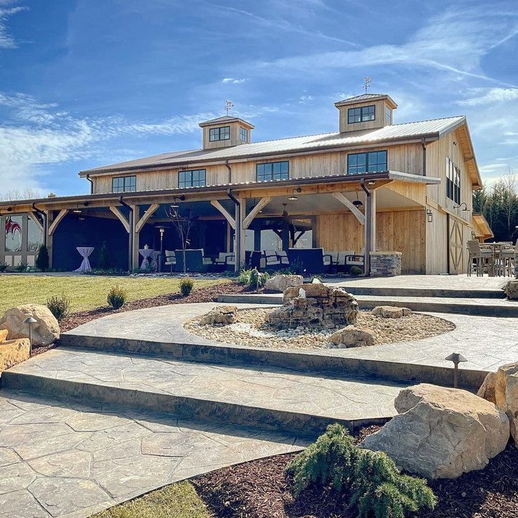 Rustic wooden barn-style building with covered porch and landscaped stone courtyard under a blue sky