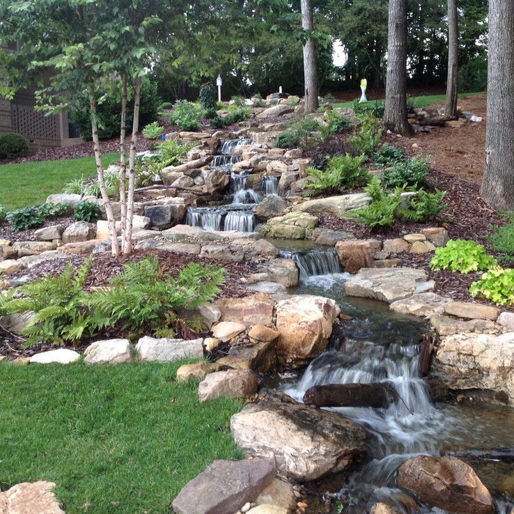 Tiered backyard waterfall flowing over rocks and plants beside a green lawn