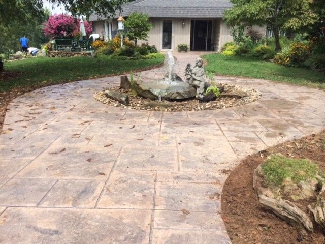 Stone garden path leading to a central fountain and house entrance, bordered by hedges and plants