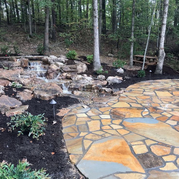 Stone patio beside a small waterfall and pond in a wooded garden