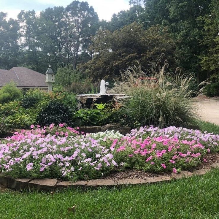 Flower bed with pink blooms, tall grasses, and a small fountain in a landscaped garden.