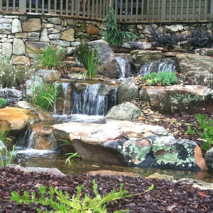 Rock garden waterfall with cascading water, stone ledges, and green plants in a landscaped yard