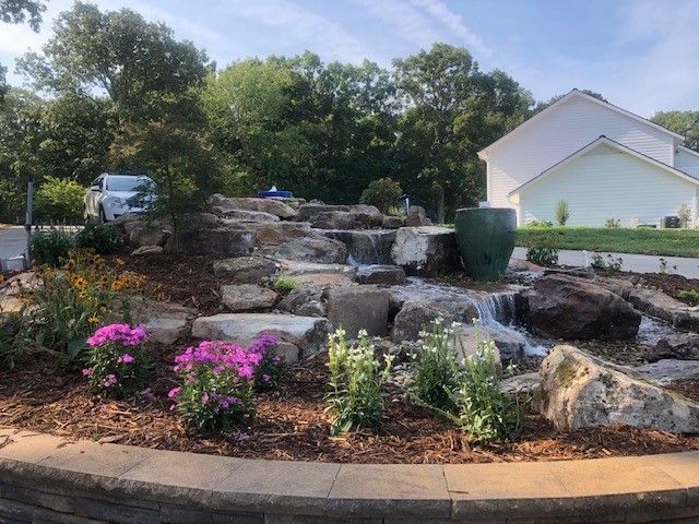 Rock garden with stone steps, pink flowers, and a white house in the background