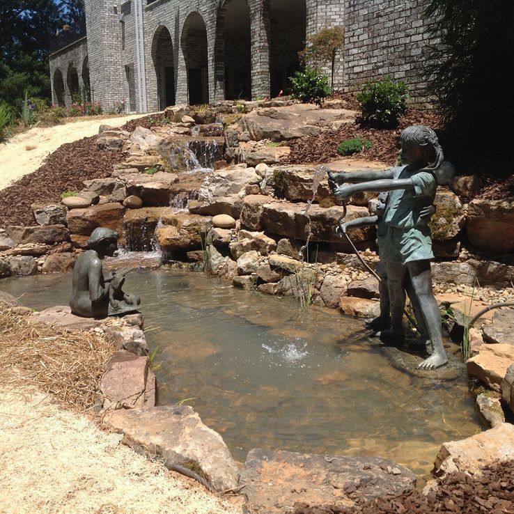Bronze children statues by a small rock waterfall in a courtyard garden