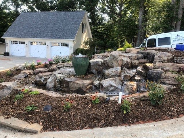 Stone terraced landscaping in front of a beige house and garage, with a white van parked nearby.