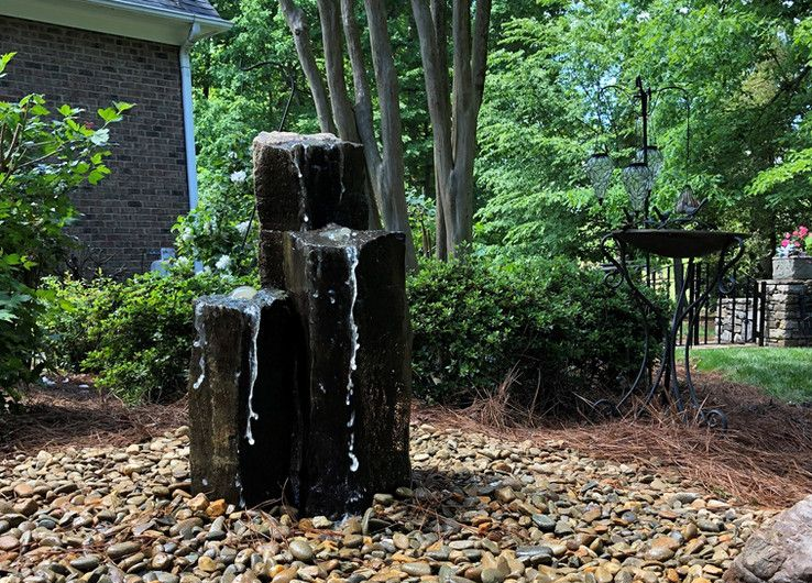 Small rock waterfall fountain in a landscaped garden with trees and shrubs