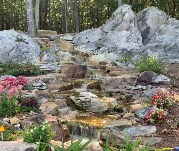 Rock waterfall in a landscaped garden with flowers and trees