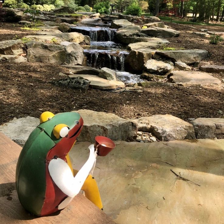 Green frog sculpture near a small waterfall in a rocky garden