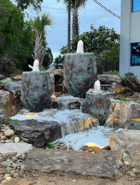 Tiered stone waterfall fountain in a landscaped garden beside a building
