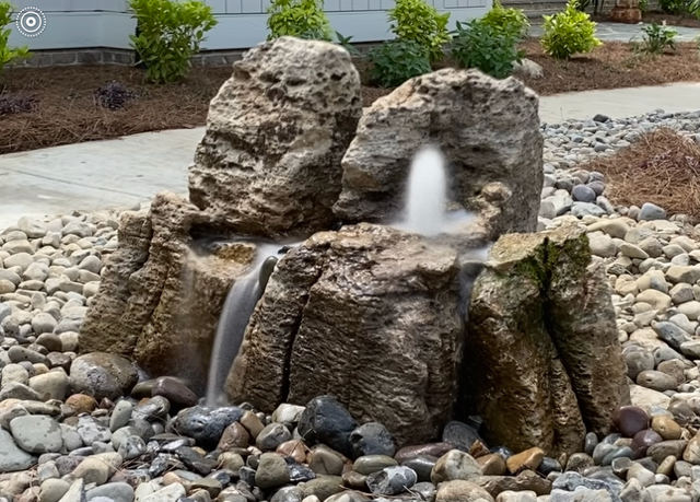 Rock waterfall fountain with water flowing between stacked stones in a landscaped garden