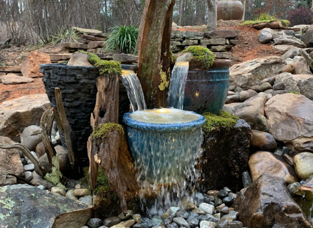 Rustic garden fountain with flowing water over blue and black stone basins among rocks and trees