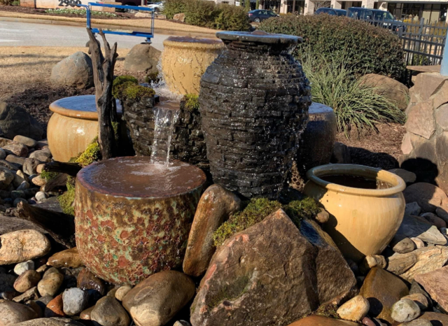 Decorative garden fountain with stacked stone and ceramic pots among rocks, water trickling down.