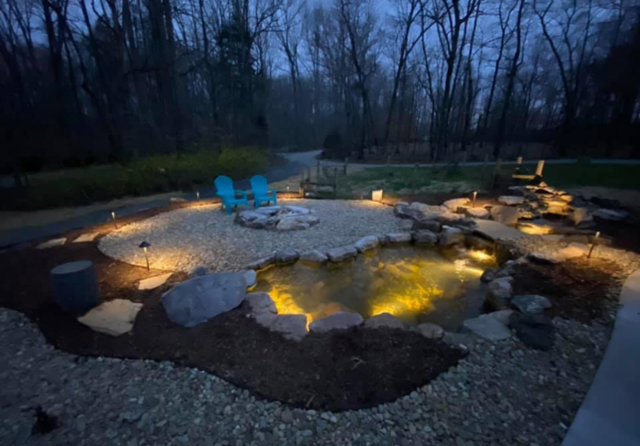 Backyard fire pit with glowing lights, stone seating, and two blue chairs at dusk
