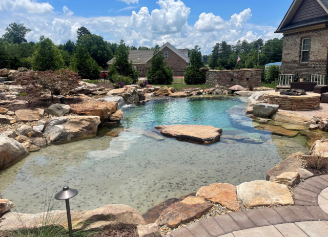 Backyard stone-lined swimming pool with clear blue water and rock landscaping under a sunny sky