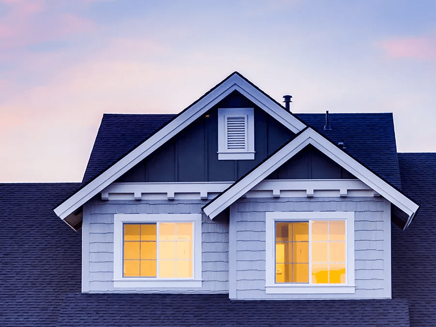 A house with a black roof and a lot of windows is lit up at night.