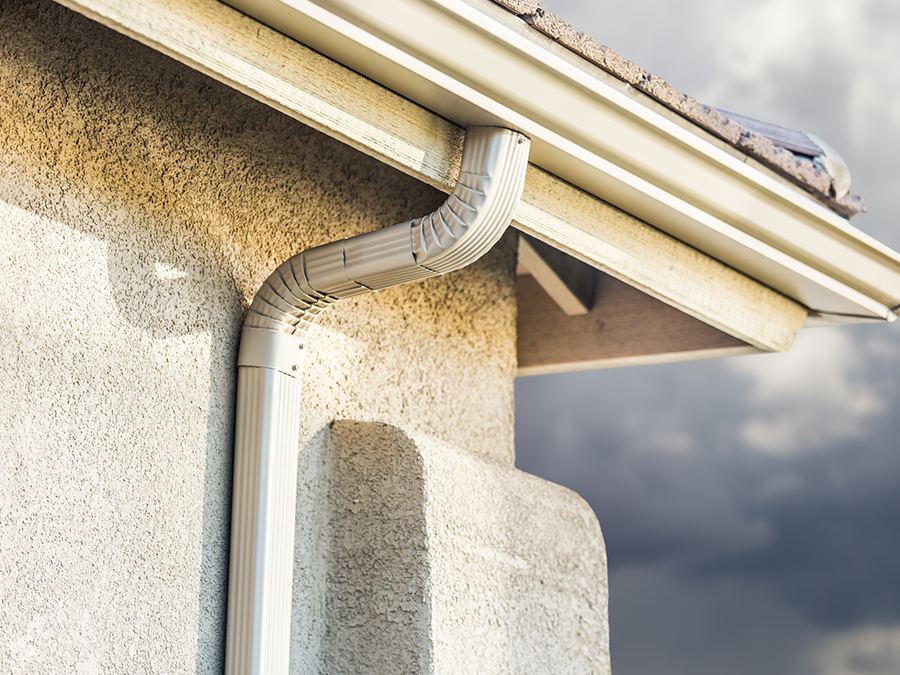 A white gutter on the side of a house with a cloudy sky in the background.