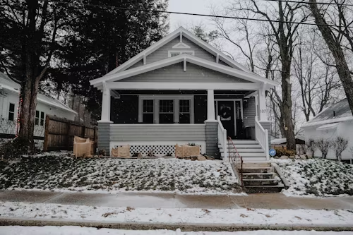 Gray house with porch and steps in a snowy yard.