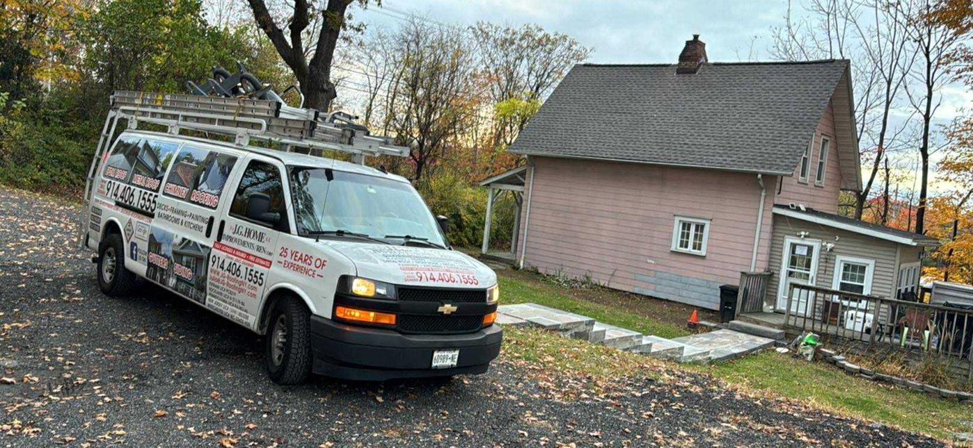 A white service van parked in front of a pink house on a hill with fall foliage.