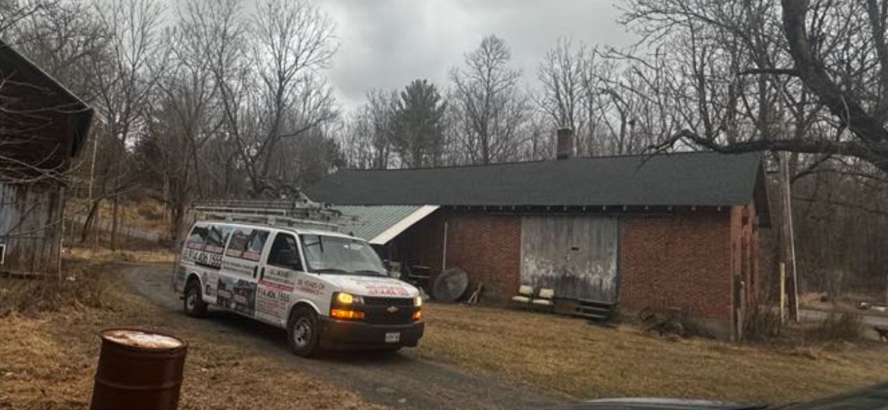 A white service van is parked near a red brick building with a dark roof. Bare trees in the background.