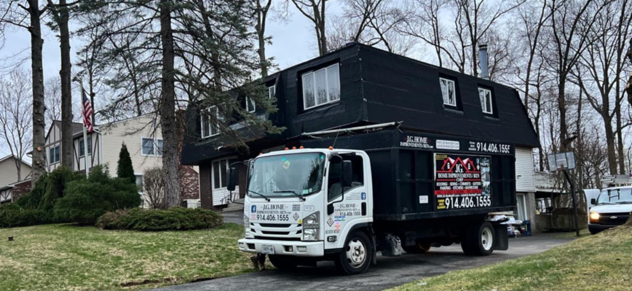 A black truck in front of a house. The house has a black roof and white windows. Trees surround the house.