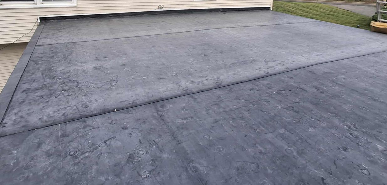 Dark gray flat roof with seams, next to a white building.
