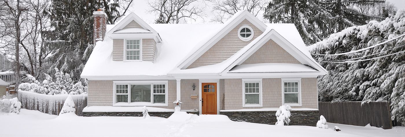 A snow-covered house with an orange front door, surrounded by snow-laden trees.