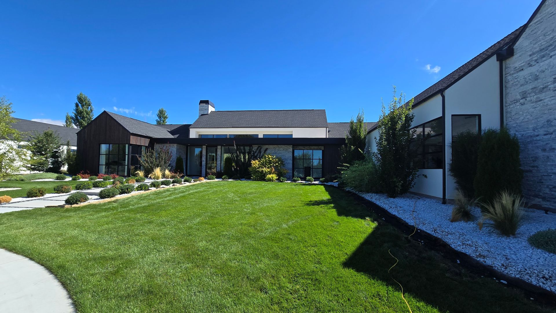 Lush green yard with landscaping leading to a modern house under a bright blue sky.