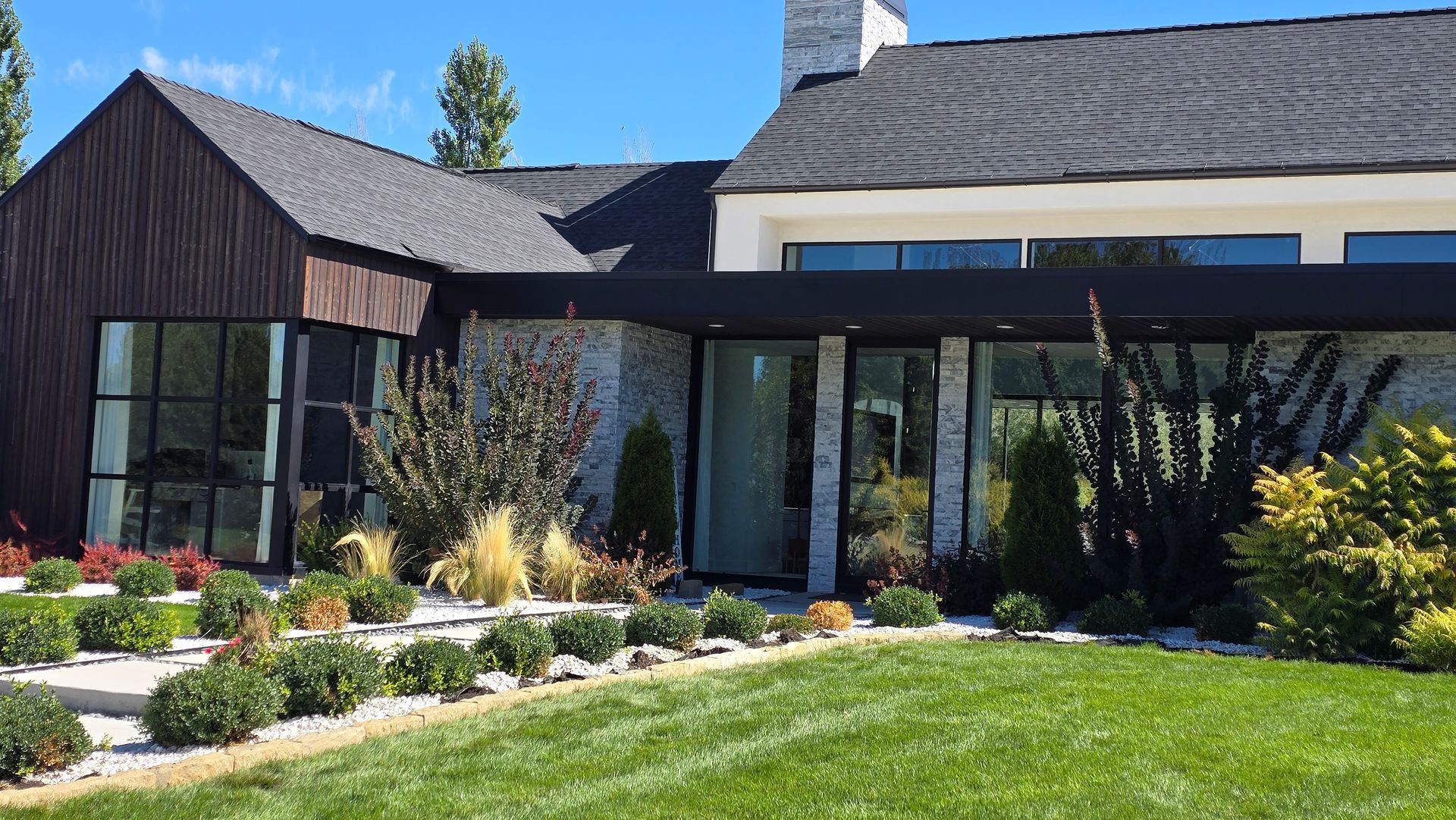 Modern home exterior with dark wood siding, stone accents, black roof, and manicured landscaping.