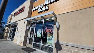 Exterior of a Jersey Mike's Subs restaurant storefront with large glass windows and an awning.
