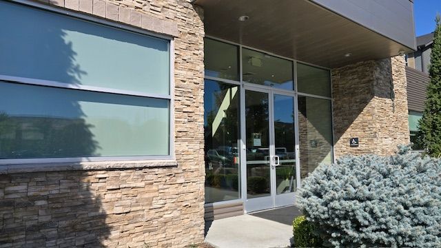 Building entrance with glass doors, stone facade, and a blue bush.