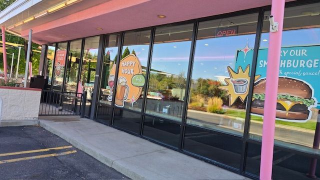 A pink-trimmed restaurant with large windows, advertisements for food, and a view of the street outside.