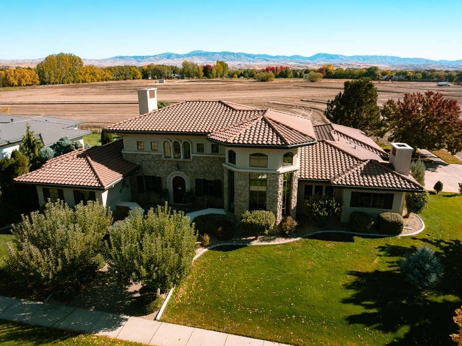 Large home with red-tile roof and green lawn, viewed from above, with fields and mountains in the background.