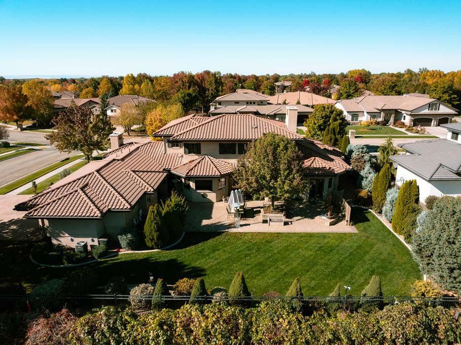 Aerial view of a large, brown-tiled roof house with a green lawn and autumn trees in a suburban setting.