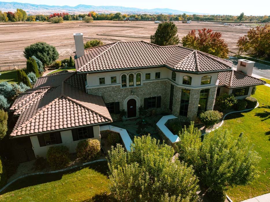 An aerial view of a large, stone-and-tile roof house with a manicured lawn.