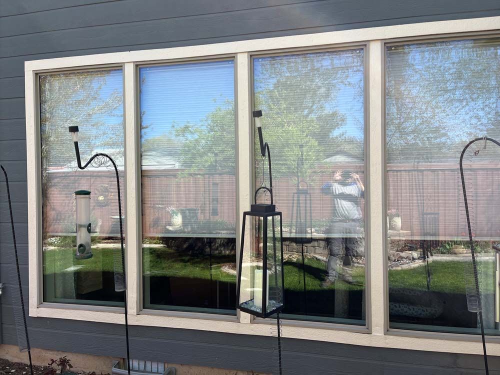 Window with bird feeders and a lantern hanging outside. Sunlight reflects on the glass and blinds.
