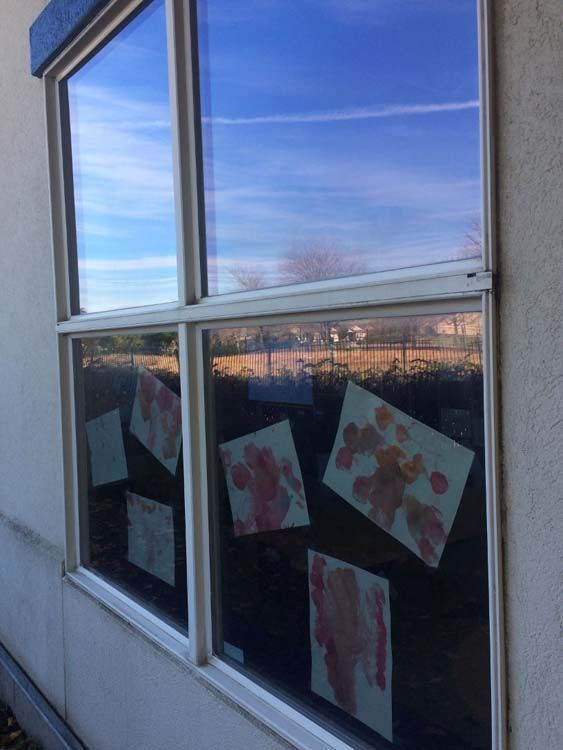 Window with child's handprint art on display. Sunny outdoor scene reflected in the glass.