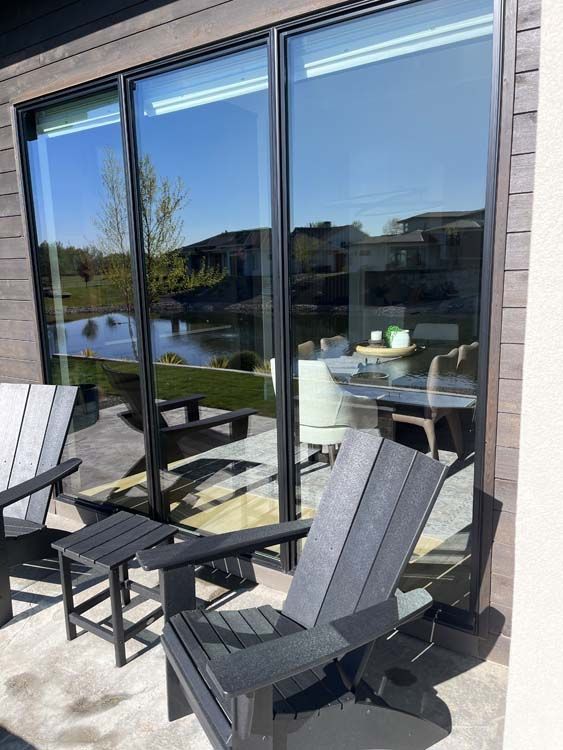 Patio with black chairs and a side table, overlooking a lake, reflected in large windows.