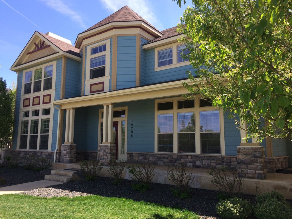 Blue two-story house with stone accents, windows, and porch under a bright sky.