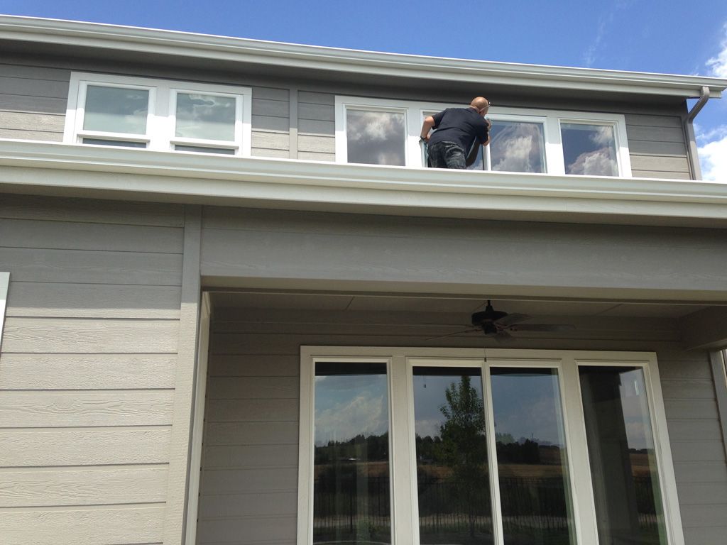 Person cleaning windows on a two-story house with gray siding.